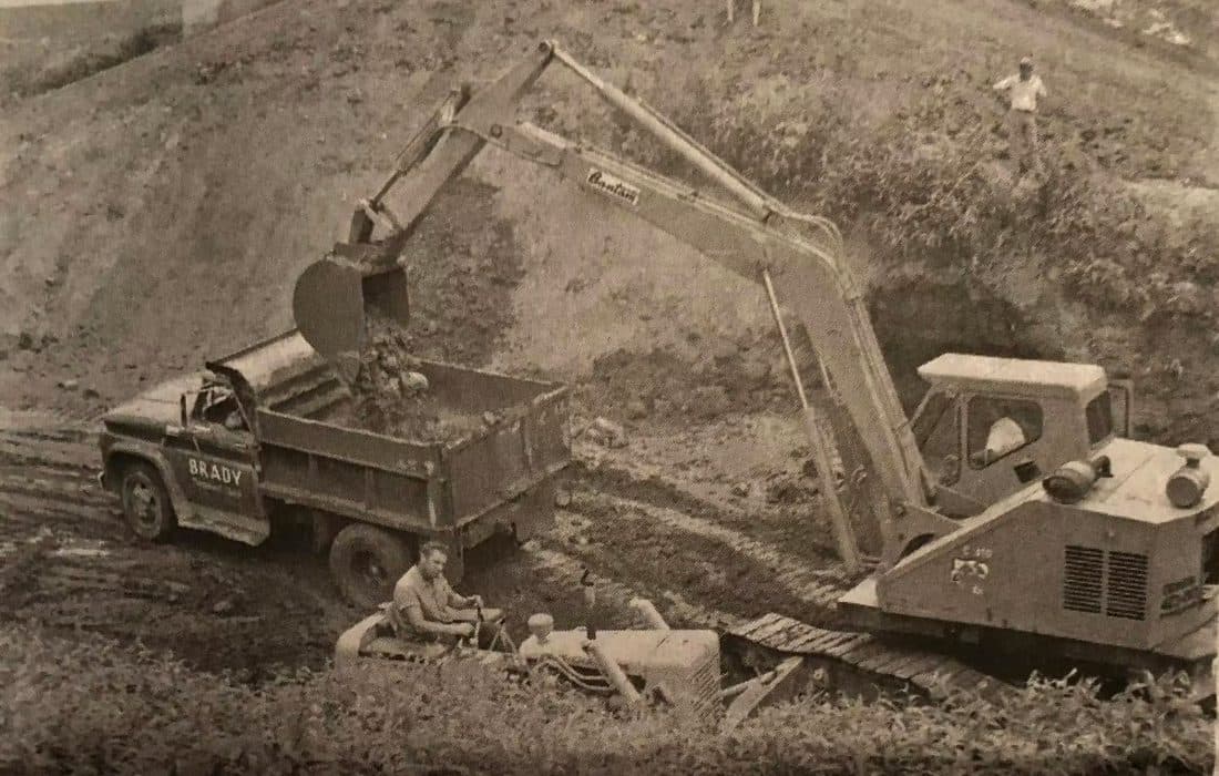 Vintage newspaper photo of an early Brady Sand & Gravel truck and Bantam excavator building a dam embankment