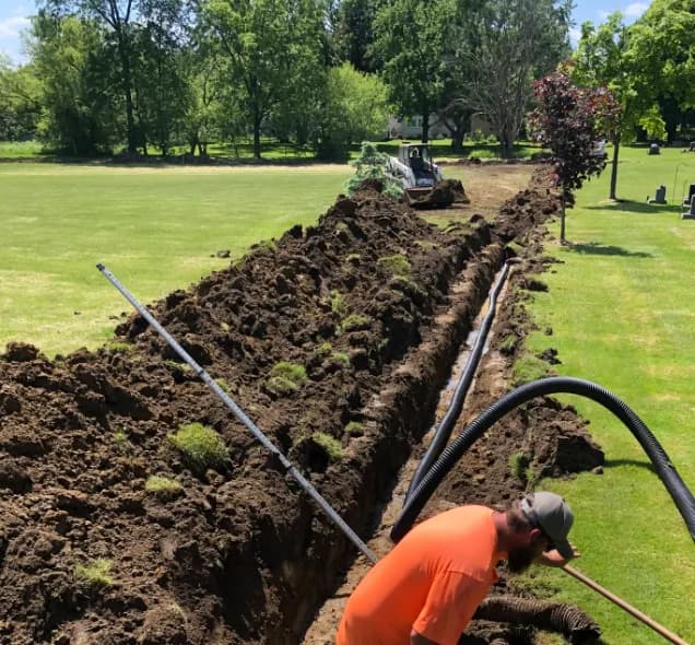 Brady crew installing drainage pipe in a trench across a lawn with a skid steer