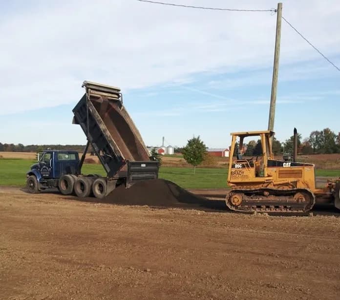 Brady dump truck spreading asphalt millings for a driveway while a CAT dozer grades
