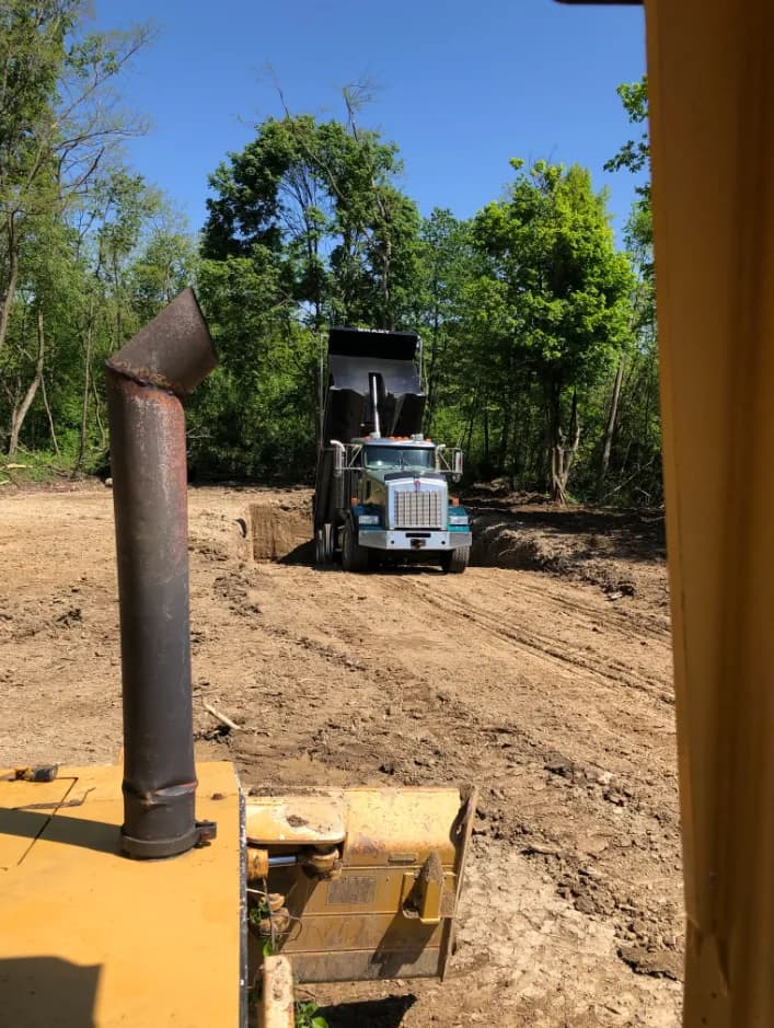 Brady dump truck delivering fill during wooded lot clearing, seen from the dozer